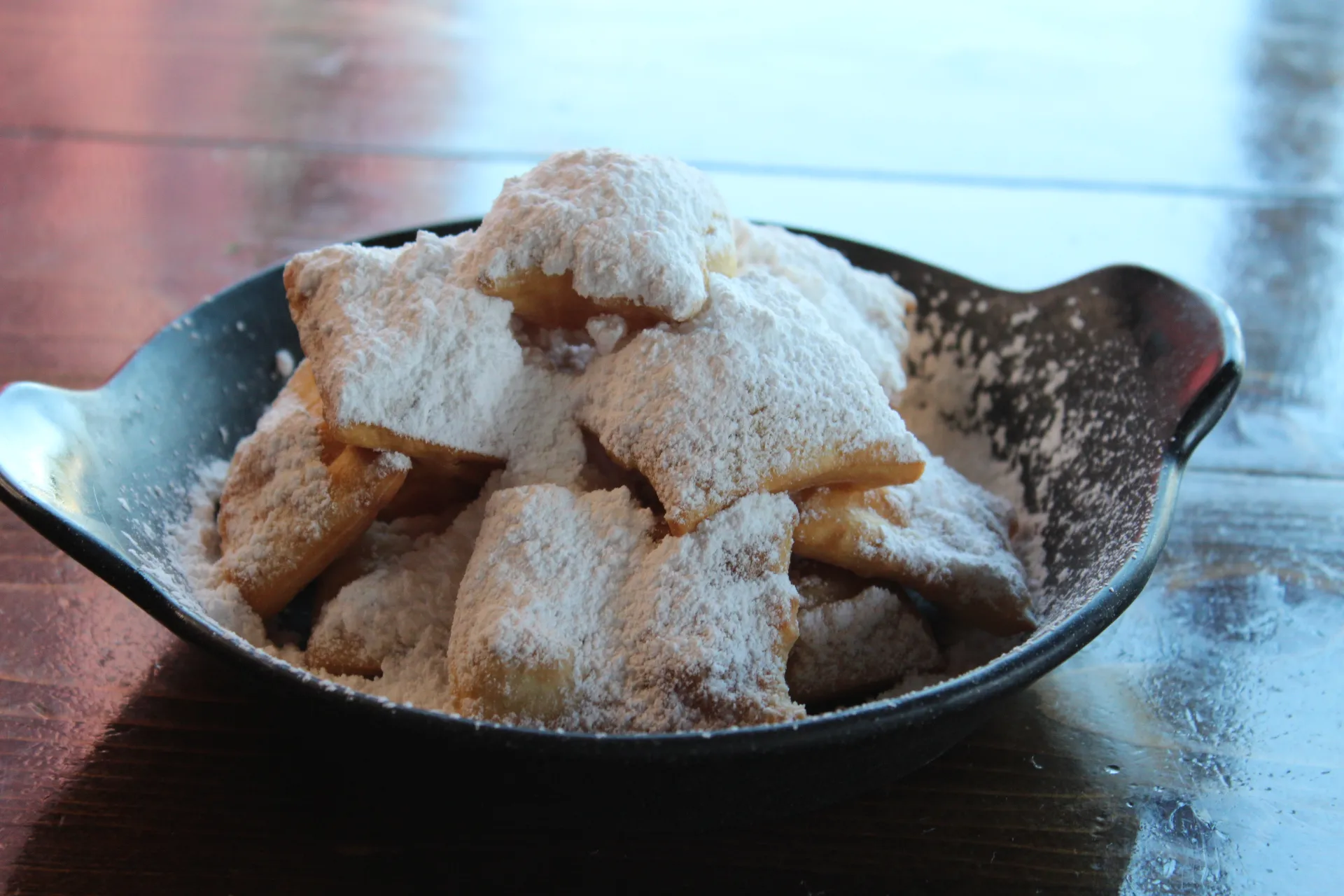 Beignet Bites Golden beignet bites dusted with powdered sugar in a black bowl, ready to be enjoyed.