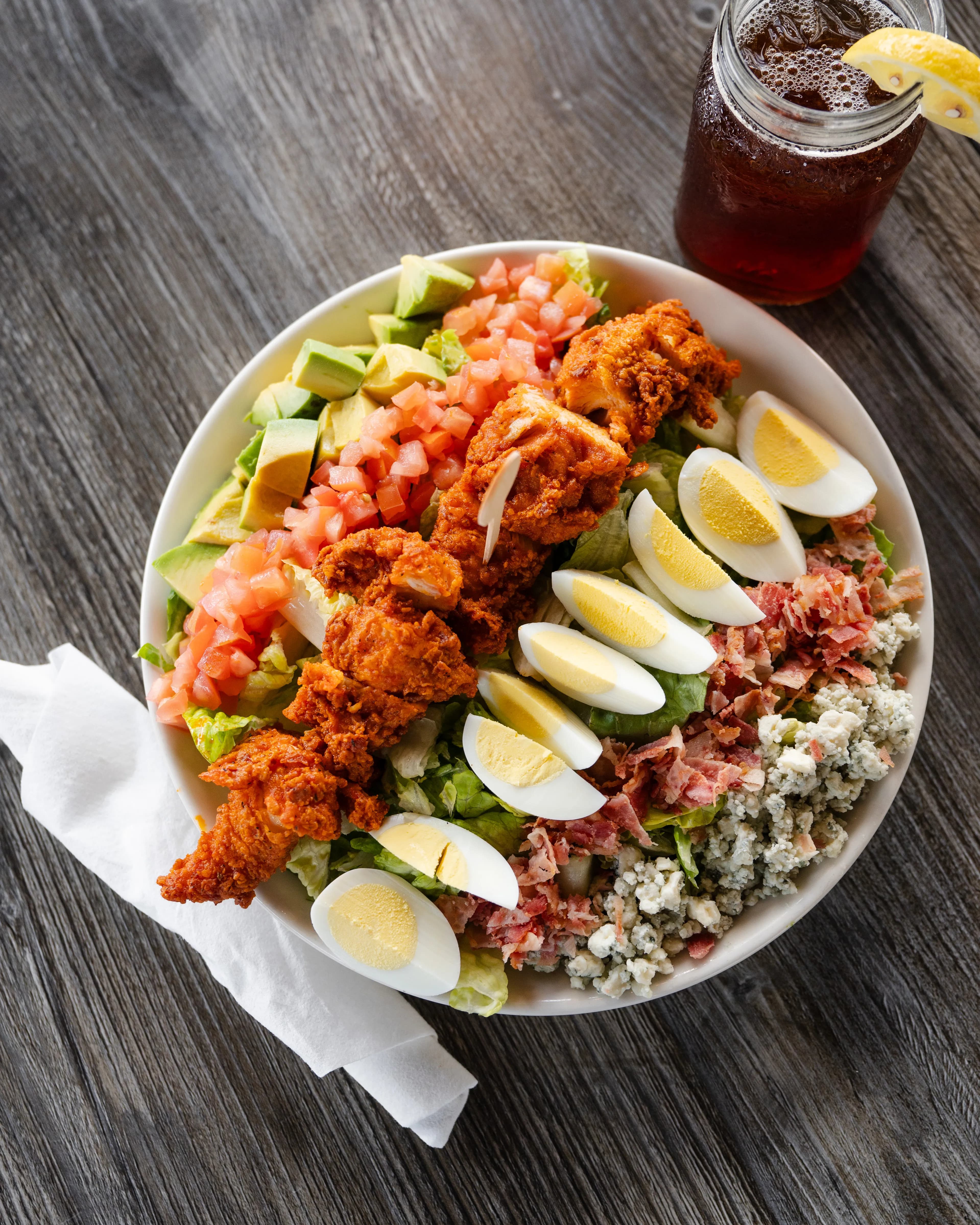 Cobb Salad A vibrant cobb salad featuring crispy fried chicken, hard-boiled eggs, bacon, blue cheese, avocado, and diced tomatoes