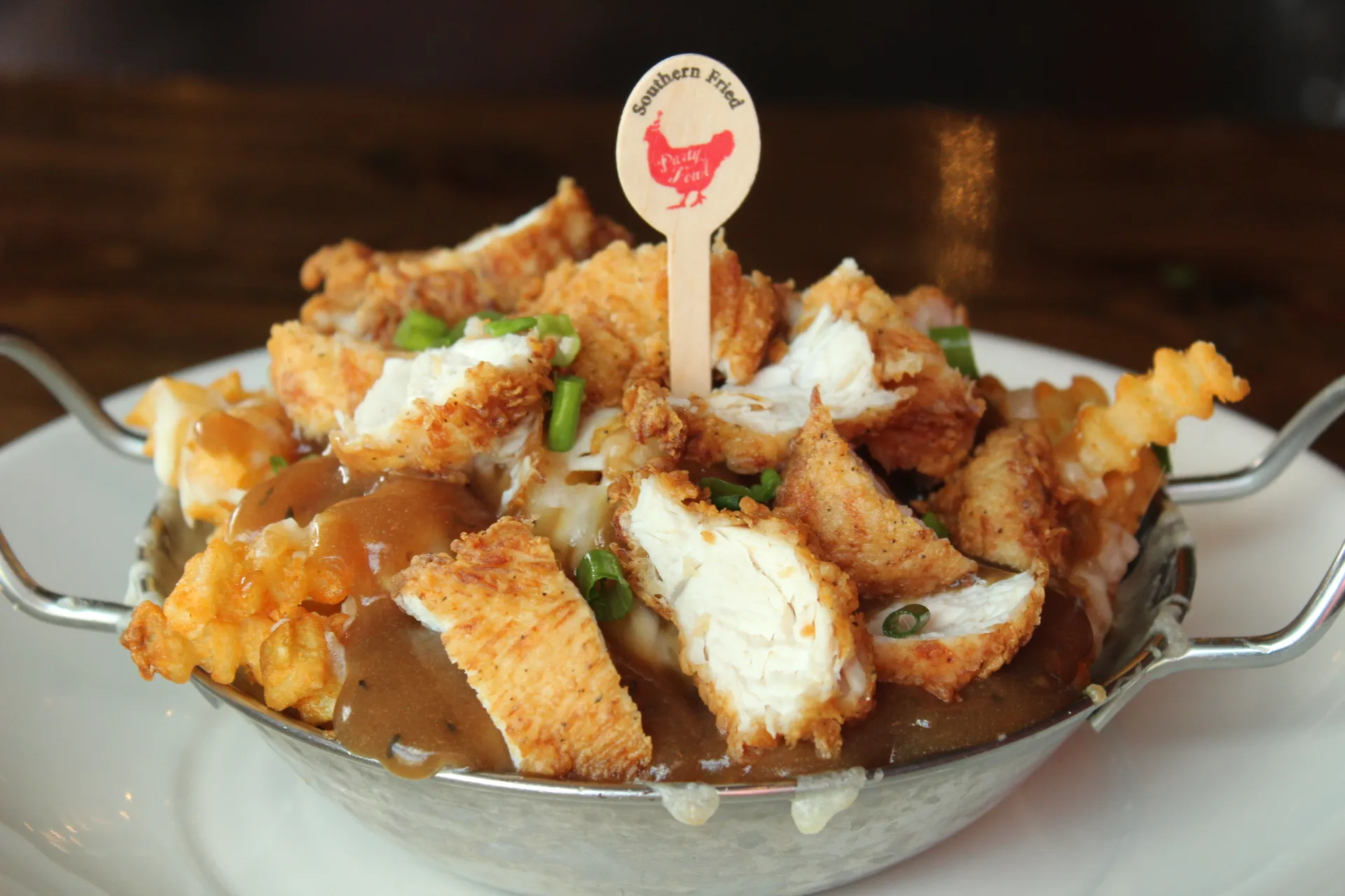 Hot Chicken Poutine Fried chicken pieces with gravy and cheese curds in a metal bowl.