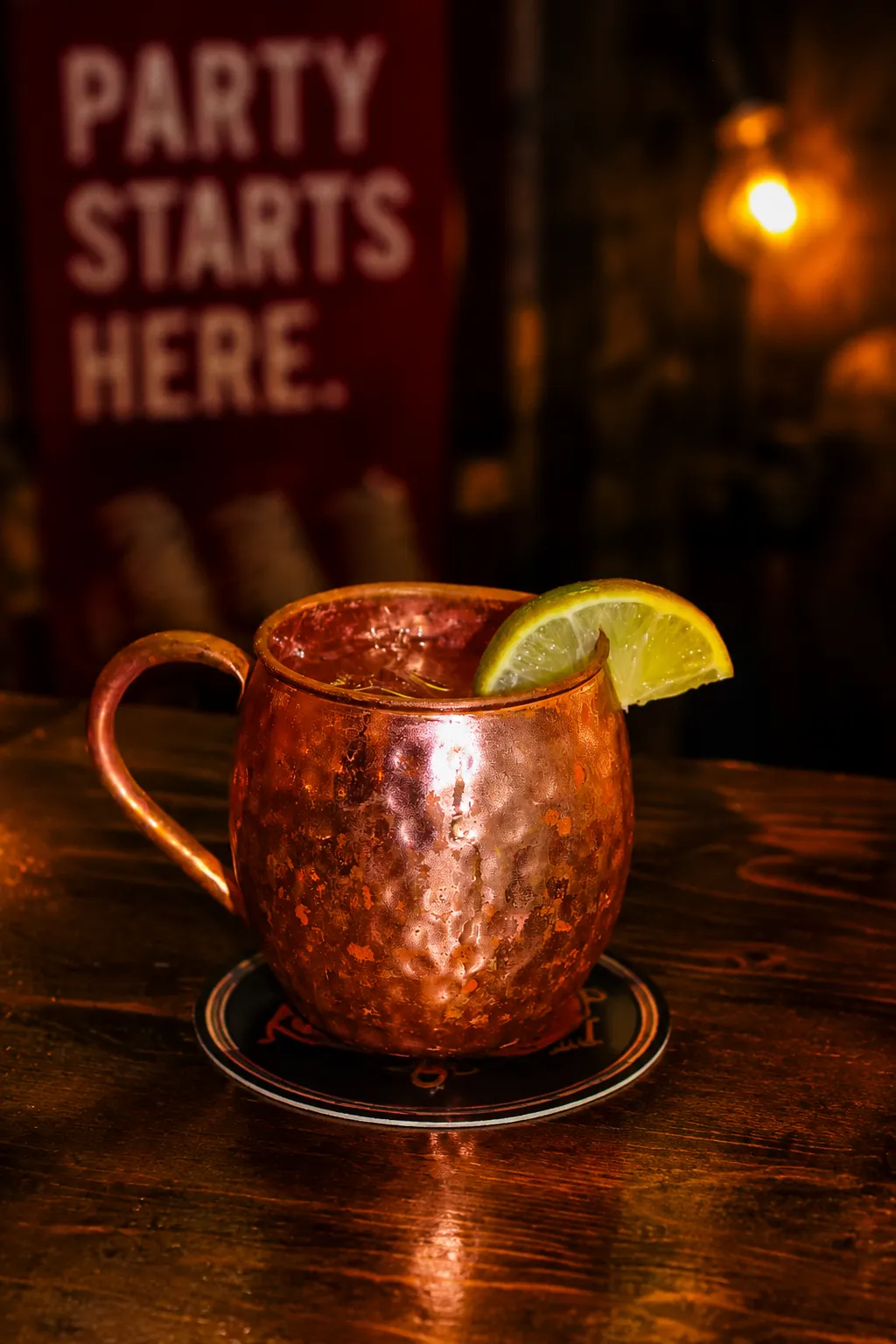 Mule A copper mug filled with a cocktail and garnished with a lemon slice, set against a warm, inviting bar backdrop.
