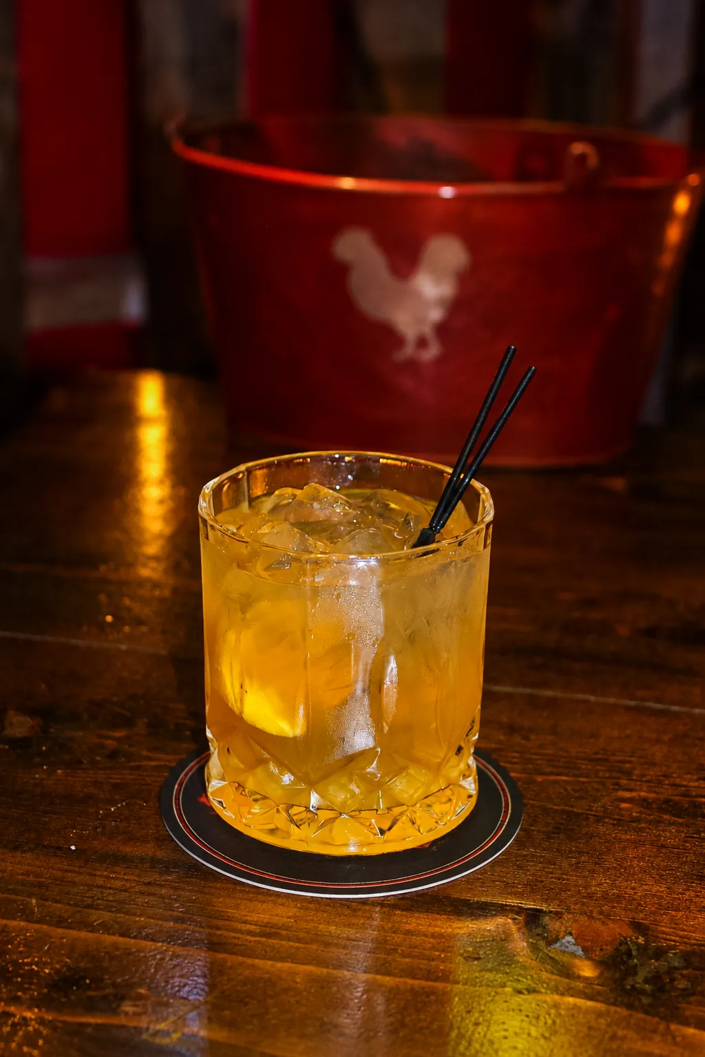 Whiskey Smash A refreshing cocktail with ice and a black straw, served in a glass on a wooden bar counter.