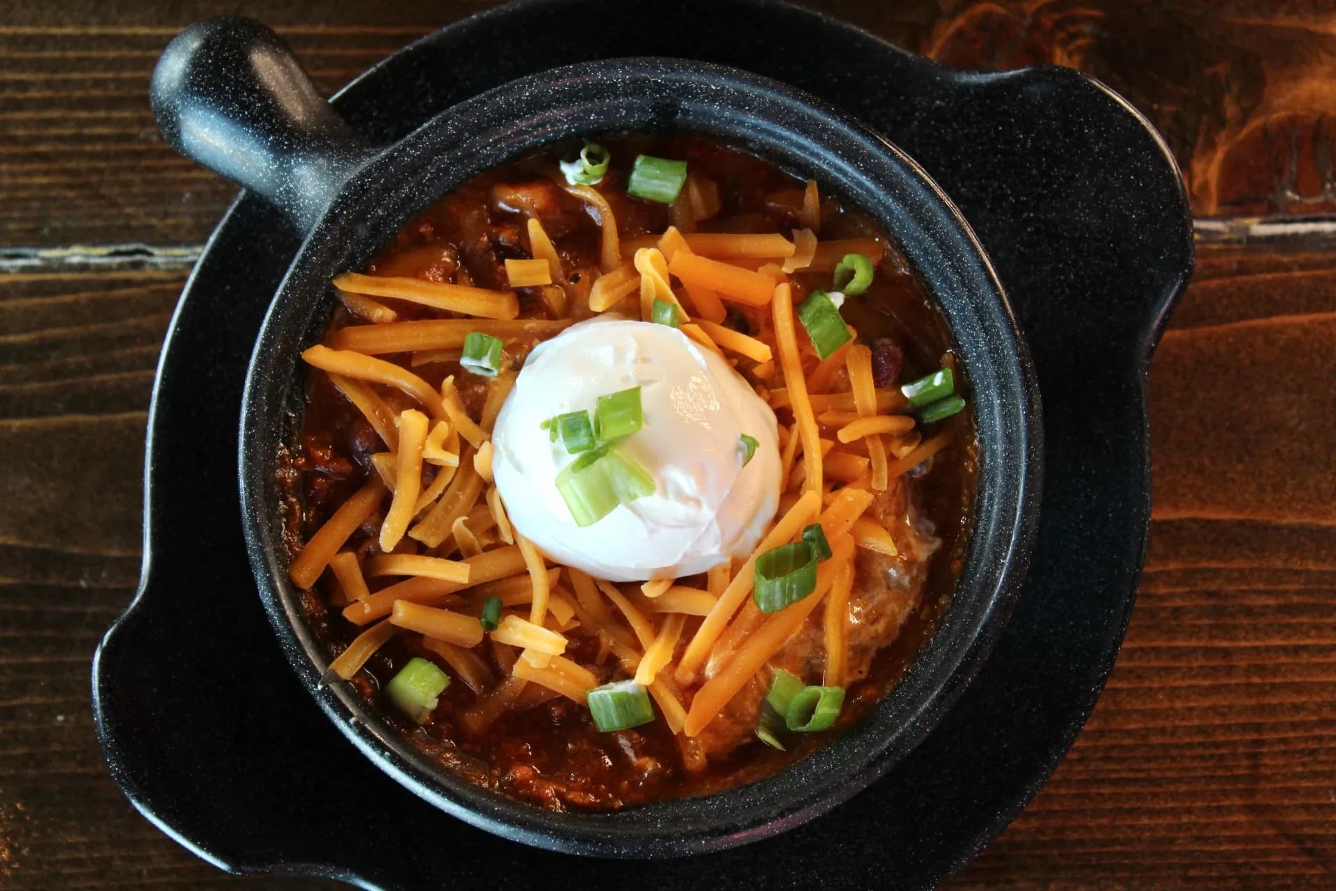Brisket Chili A hearty bowl of chili topped with shredded cheese, sour cream, and chopped green onions.