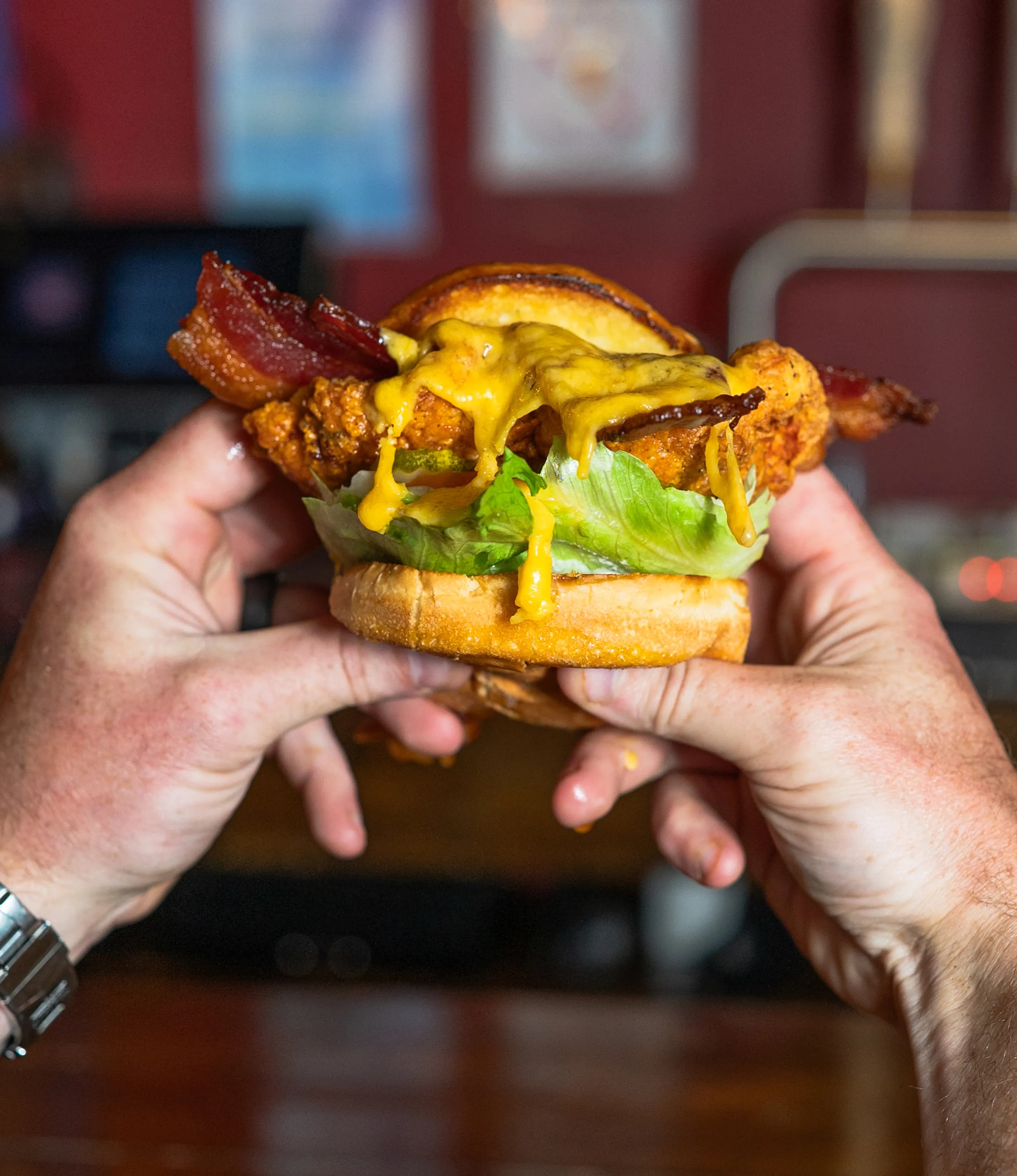 Chickenncheddar A hand holding a juicy chicken burger topped with melted cheddar cheese, crispy bacon, and fresh lettuce.