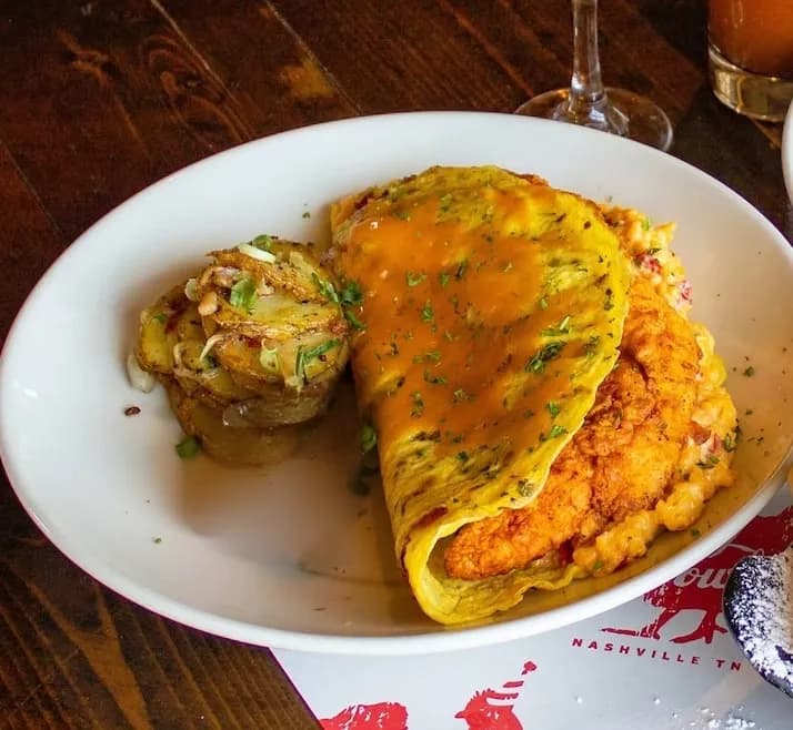 Pimento Cheese Omelette A delicious pimento cheese omelette served with roasted potatoes and a side of sauce, garnished with herbs.